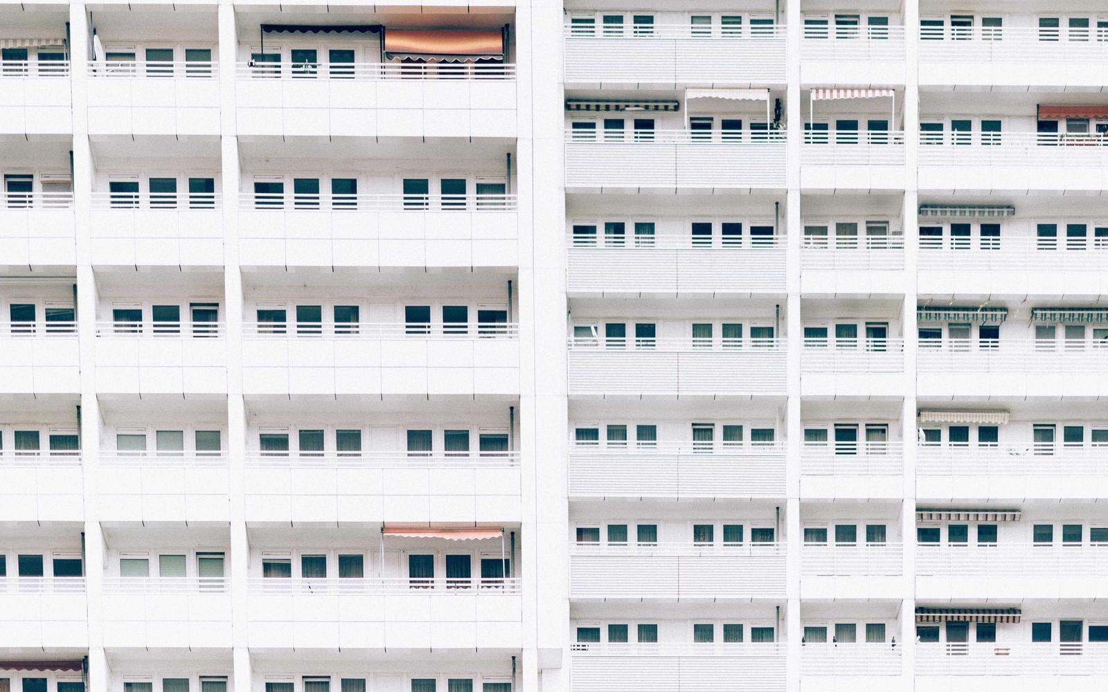 A white apartment block facade with repeating balconies and windows